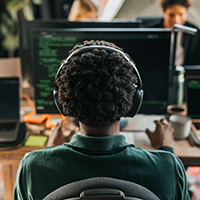 A person with curly hair and headphones coding on a computer screen, seen from the back.